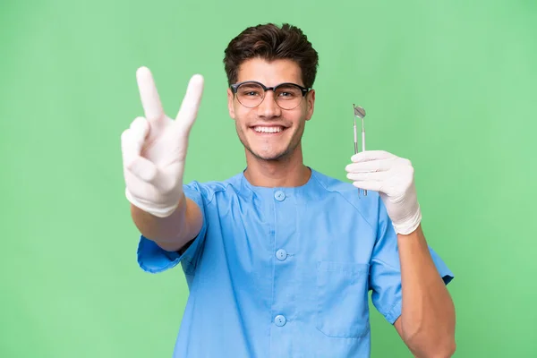 Young Dentist Man Holding Tools Isolated Background Smiling Showing Victory — Stock Photo, Image