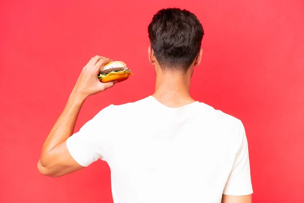 Jonge Blanke Man Met Een Hamburger Geïsoleerd Rode Achtergrond Achterste — Stockfoto