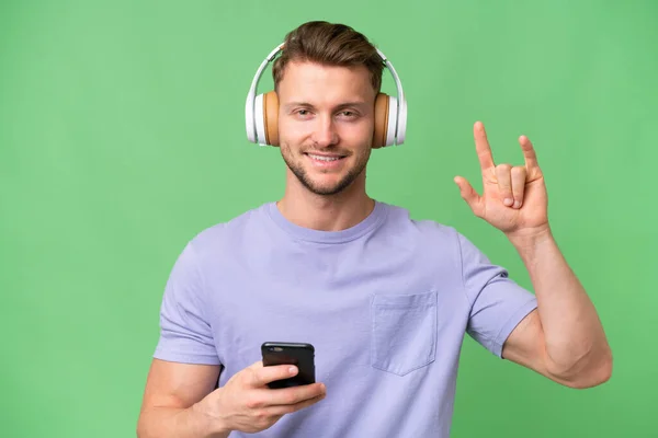 Young Blonde Caucasian Man Isolated Background Listening Music Mobile Making — Stock Photo, Image