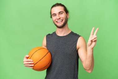 İzole edilmiş arka planda genç basketbolcu gülümsüyor ve zafer işareti gösteriyor.