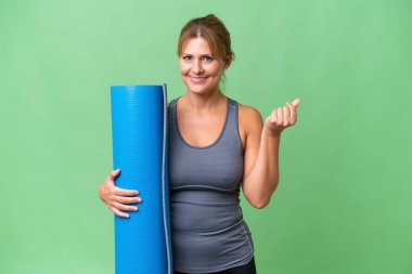 Orta yaşlı sporcu bir kadın, yoga derslerine giderken elinde paspas tutarak para hareketi yapıyor.