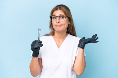 Orta yaşlı Dişçi, mavi arka plan üzerinde araçlar tutuyor.