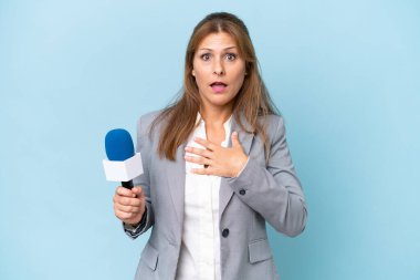 İzole edilmiş mavi arka planda orta yaşlı televizyon sunucusu kadın sağa bakarken şaşırdı ve şok oldu.