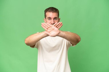 Yeşil krom arka planda izole edilmiş yakışıklı beyaz bir adam bir hareketi durdurmak için eliyle jesti durduruyor.