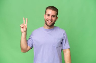 Yeşil krom arka planda izole edilmiş yakışıklı beyaz adam gülümsüyor ve zafer işareti gösteriyor.