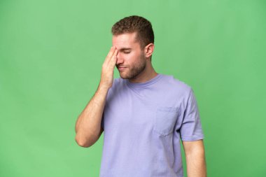 Genç, yakışıklı, beyaz adam yeşil krom arka planda izole edilmiş, baş ağrısı var.