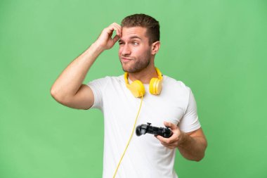 Yeşil krom arka planda izole edilmiş bir video oyunu kontrolörüyle oynayan genç yakışıklı adamın şüpheleri ve kafa karıştırıcı bir yüz ifadesi var.