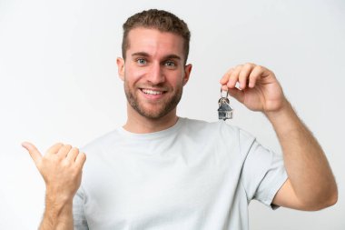 Beyaz arka planda izole edilmiş ev anahtarlarını elinde tutan genç beyaz bir adam kendinden emin bir ifadeyle sana parmak basıyor.