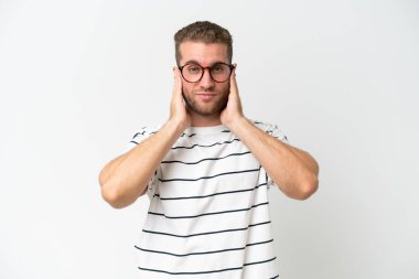 Beyaz arka planda izole edilmiş yakışıklı beyaz adam hayal kırıklığına uğramış ve kulaklarını kapatmış.