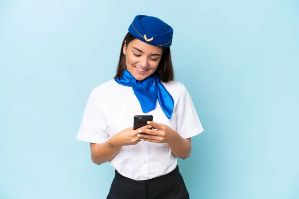 青い背景に隔離された飛行機スチュワーデス原因アジアの女性は 携帯電話でメッセージを送信します — ストック写真