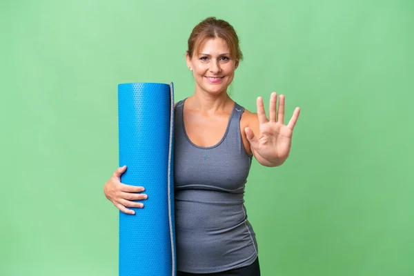中年妇女去上瑜伽课 同时拿着垫子盖住孤立的背景 用手指数着5 — 图库照片