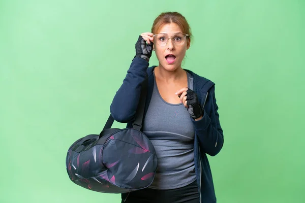 中年スポーツ女性でスポーツバッグ上の隔離された背景に眼鏡と驚き — ストック写真