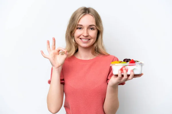 stock image Young English woman holding a bowl of fruit over isolated white background showing ok sign with fingers