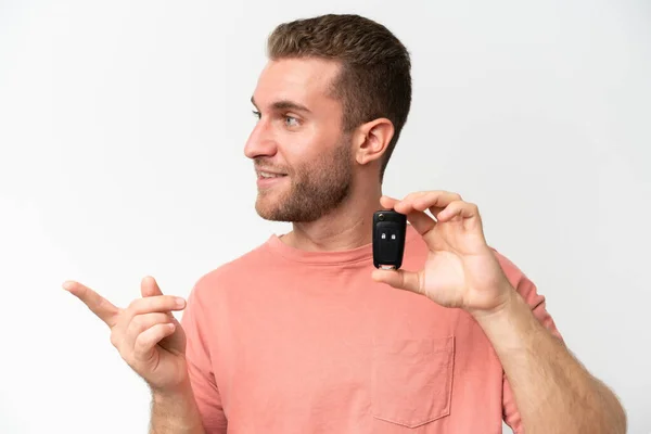 Stock image Young caucasian man holding car keys isolated on white background pointing to the side to present a product