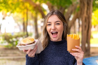 Genç ve güzel Romen kadın açık havada hamburger ve patates kızartması tutuyor