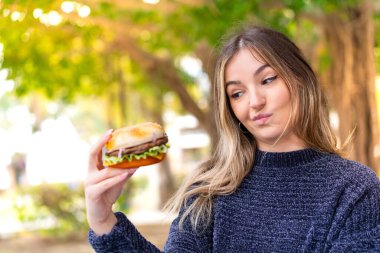 Genç ve güzel Romen kadın elinde burgerle dışarıda üzgün bir ifadeyle.
