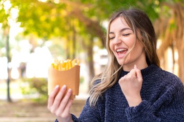 Genç, güzel Romen kadın açık havada patates kızartması tutuyor ve zaferi kutluyor