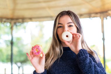 Genç ve güzel Romen kadın açık havada donut tutuyor.