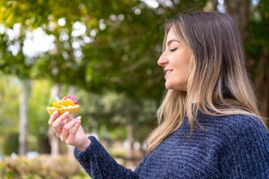 Genç, güzel Romen bir kadın açık havada neşeli bir ifadeyle tart tutuyor.