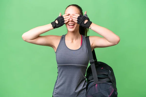 年轻的女运动员 手拿着运动包 遮住孤立的背景 用手捂住眼睛 — 图库照片