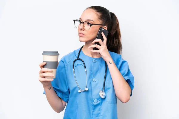 年轻的高加索外科医生妇女 被隔离在白人背景下 手里拿着咖啡和手机 — 图库照片