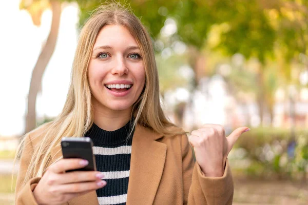 Joven Mujer Rubia Bonita Aire Libre Utilizando Teléfono Móvil Apuntando —  Fotos de Stock