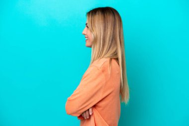 Genç Uruguaylı kadın mavi arka planda yan pozisyonda izole edilmiş.