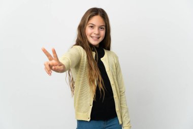 Küçük kız izole edilmiş beyaz arka planda gülümsüyor ve zafer işareti gösteriyor.