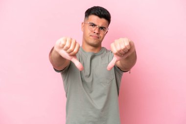 Pembe arka planda soyutlanmış, iki eliyle baş parmağını gösteren beyaz tenli yakışıklı bir adam.