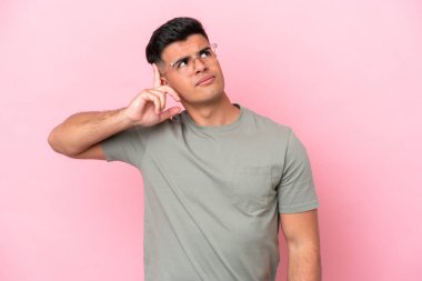 Pembe arka planda soyutlanmış beyaz, yakışıklı bir adam deliliğin jestini yapıyor. Parmağını kafaya koyuyor.