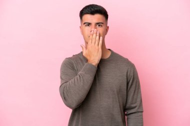 Beyaz tenli yakışıklı bir adam pembe arka planda izole edilmiş. Ağzını eliyle kapatıyor.
