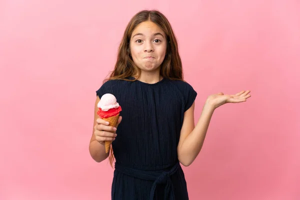 手を上げながら疑問を持っている隔離されたピンクの背景の上にコーンアイスクリームを持つ子供 — ストック写真