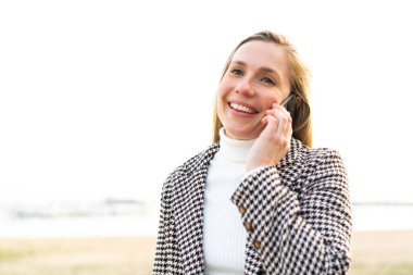 Dışarıdaki genç sarışın kadın cep telefonuyla sohbet ediyor.