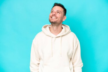 Kafkasyalı yakışıklı genç adam mavi arka planda izole edilmiş bir şekilde yukarı bakarken bir fikir düşünüyor.