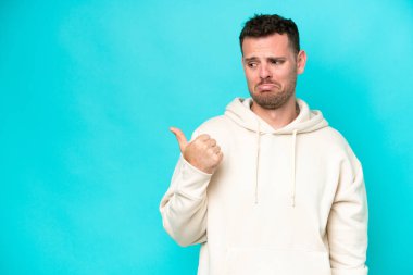 Mavi arka planda izole edilmiş genç, beyaz, yakışıklı bir adam mutsuzdu ve yüzünü gösteriyordu.