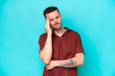 Kafkasyalı yakışıklı genç adam mavi arka planda başağrısı ile izole edilmiş.