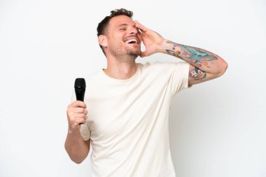 Beyaz arka planda izole edilmiş bir mikrofonu eline alan beyaz tenli şarkıcı çok gülümsüyor.