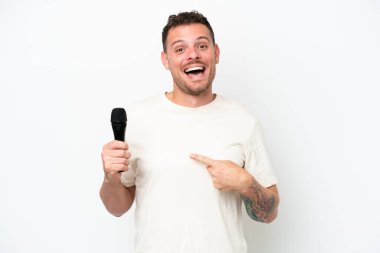 Beyaz arka planda, sürpriz bir yüz ifadesiyle izole edilmiş bir mikrofonu kaldıran beyaz tenli genç bir şarkıcı.