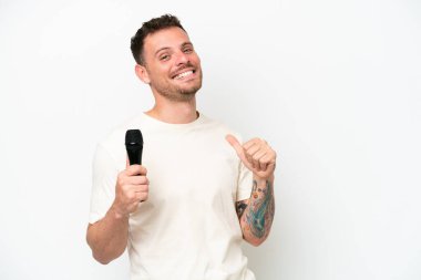 Beyaz arka planda izole edilmiş, gururlu ve kendini beğenmiş bir mikrofonu eline alan Kafkasyalı genç şarkıcı.