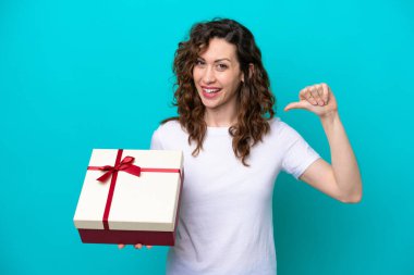 Mavi arka planda, gururlu ve kendini beğenmiş bir hediyeyi elinde tutan beyaz bir kadın.