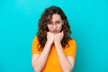 Mavi arka planda, gözlüklü ve yorgun genç beyaz kadın.