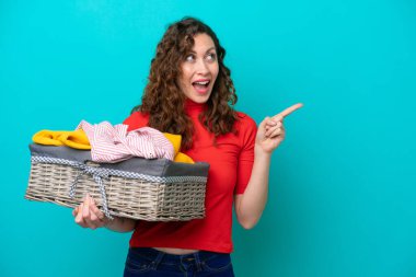 Kafkasyalı genç bir kadın mavi arka planda izole edilmiş bir çamaşır sepetini tutuyor. Çözümün farkına varmak için parmağını kaldırıyor.