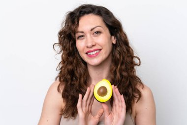 Beyaz arka planda izole edilmiş beyaz bir kadın elinde bir avokado tutarken gülümsüyor. Portreyi kapat