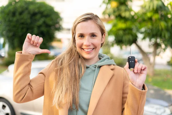 Νεαρή Ξανθιά Γυναίκα Κρατώντας Κλειδιά Του Αυτοκινήτου Εξωτερικούς Χώρους Υπερήφανη — Φωτογραφία Αρχείου