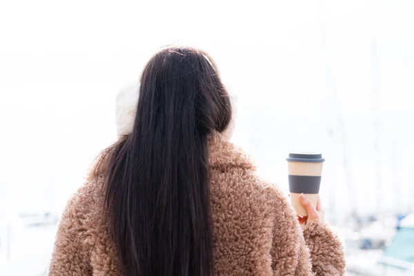 年轻女子穿着冬衣 背着咖啡站在室外 — 图库照片
