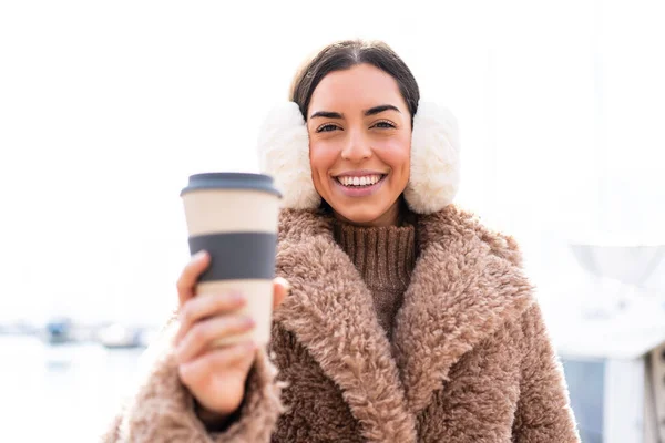 年轻女人穿着冬衣 拿着咖啡 满面春风地在户外喝咖啡 — 图库照片