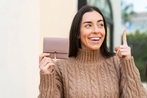 指を持ち上げながら解決策を実現しようと屋外で財布を持っている若い女性 — ストック写真