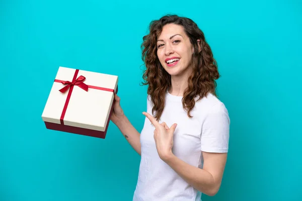 Young Caucasian Woman Holding Gift Isolated Blue Background Pointing — Stockfoto