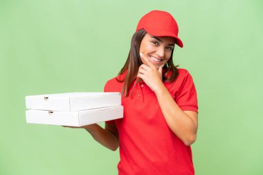 Pizza teslimatı, iş üniformalı beyaz kadın yeşil krom arka planda izole edilmiş pizza kutuları alıyor mutlu ve gülümsüyor