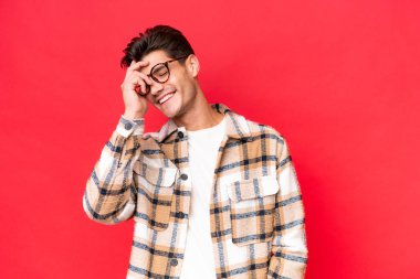 Kafkasyalı yakışıklı genç adam kırmızı arka planda izole edilmiş gülüyor.